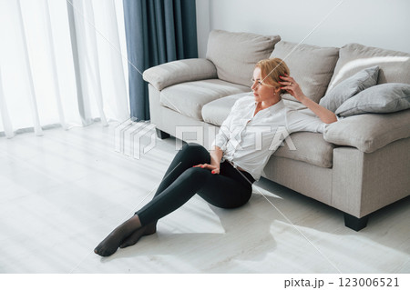 In black jeans. Woman in formal wear sitting on the floor near sofa in domestic room 123006521
