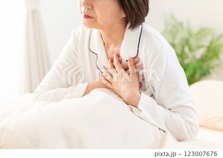 朝の寝室で胸の痛みに苦しむ白いパジャマ姿のミドル女性 123007676