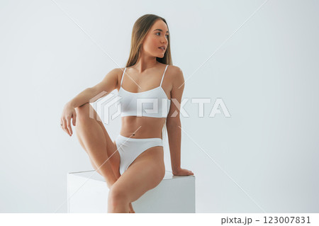 Sitting on white cube. Woman in underwear with slim body type is posing in the studio Sitting on white cube. Woman in underwear with slim body type is posing in the studio 123007831
