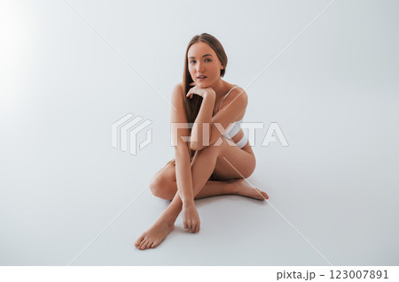 Beautiful model sitting on the floor. Woman in underwear with slim body type is posing in the studio Beautiful model sitting on the floor. Woman in underwear with slim body type is posing in the studio 123007891