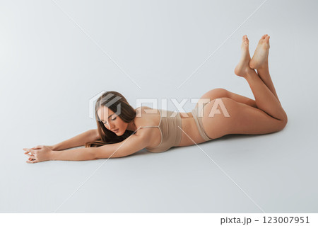 Smiling when lying down on the floor. Woman in underwear with slim body type is posing in the studio 123007951