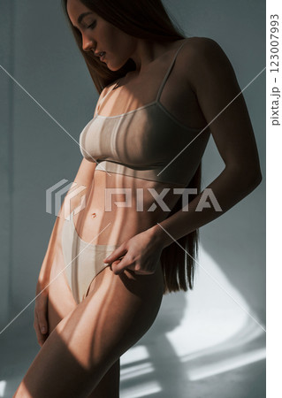 Sunlight through the windows. Woman in underwear with slim body type is posing in the studio Sunlight through the windows. Woman in underwear with slim body type is posing in the studio 123007993