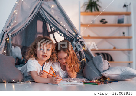 Learning to write and draw. With paper and pencils. Two little girls is in the tent in domestic room together Learning to write and draw. With paper and pencils. Two little girls is in the tent in domestic room together 123008919