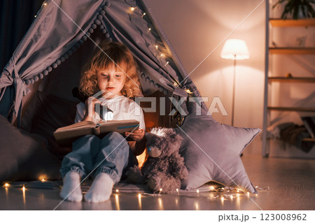 Using flashlight to read the book. Cute little girl is in the tent in domestic room Using flashlight to read the book. Cute little girl is in the tent in domestic room 123008962