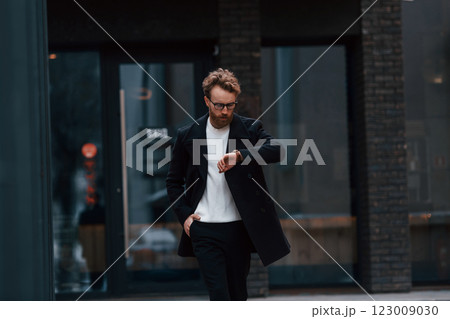 Stylish man with beard and in glasses is outdoors near building 123009030
