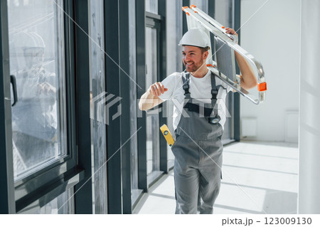 Holding ladder. Repairman is working indoors in the modern room Holding ladder. Repairman is working indoors in the modern room 123009130