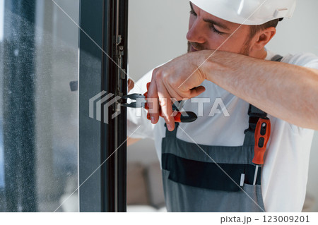 Using tool on the windows. Repairman is working indoors in the modern room Using tool on the windows. Repairman is working indoors in the modern room 123009201