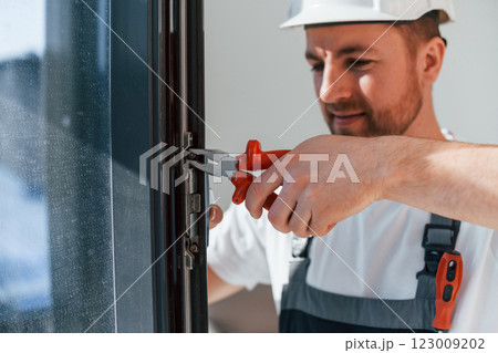 Using tool on the windows. Repairman is working indoors in the modern room Using tool on the windows. Repairman is working indoors in the modern room 123009202