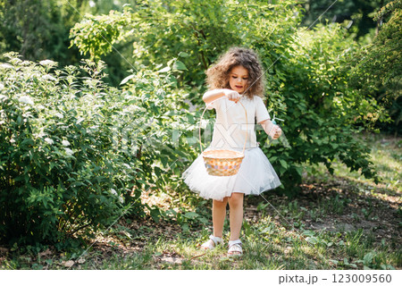 Easter egg hunt. Girl child Wearing Bunny Ears Running To Pick Up Egg In Garden. Easter tradition. Baby with basket full of colorful eggs. 123009560