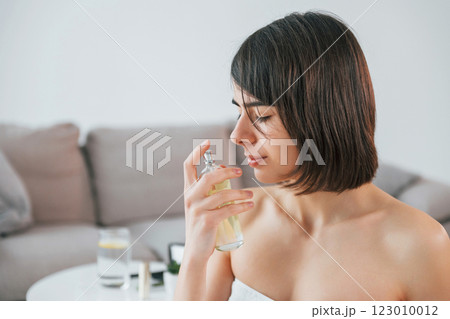 Holding glass with parfume. Young woman is at home. Conception of beauty 123010012