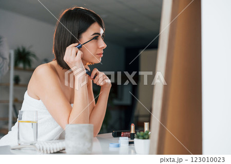 Doing eyelashes make up. Young woman is at home. Conception of beauty 123010023