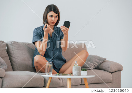 Sitting on the sofa and doing make up. Young woman is at home. Conception of beauty 123010040
