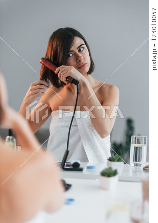 Straightening the hair. Young woman is at home. Conception of beauty Straightening the hair. Young woman is at home. Conception of beauty 123010057