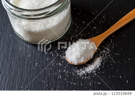 Monosodium glutamate in a wooden spoon and glass jar full of MSG over black background. 123010699