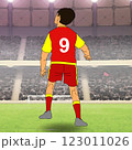 A soccer player wearing a red and yellow uniform with the number 9 is standing on a field, facing away and looking at a packed stadium. A soccer player wearing a red and yellow uniform with the number 9 is standing on a field, facing away and looking at a packed stadium. 123011026