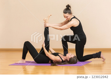 Yoga trainer is helping young woman make exercise stretching her leg at gym background. 123012042
