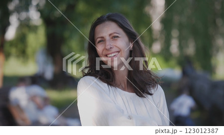 A cheerful woman with long flowing hair smiles warmly and joyfully in a bright sunny outdoor setting 123012387