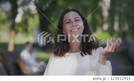 A joyful woman in a bright white outfit enjoys a sunny day in the park, radiating positivity around her 123012415