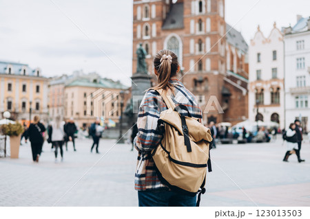 Tourist woman with backpack on Market Square in Krakow, Traveling Europe in autumn. St. Marys Basilica, cloudy day. Attractive female is exploring city. Top tourist attraction 123013503