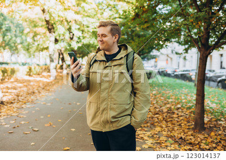 Young 30s man smiling confident using smartphone at street. Communication and gadgets, connection concept. Man holding on cell smartphone while relaxing outdoors, Urban lifestyle banner. Autumn time Young 30s man smiling confident using smartphone at street. Communication and gadgets, connection concept. Man holding on cell smartphone while relaxing outdoors, Urban lifestyle banner. Autumn time 123014137