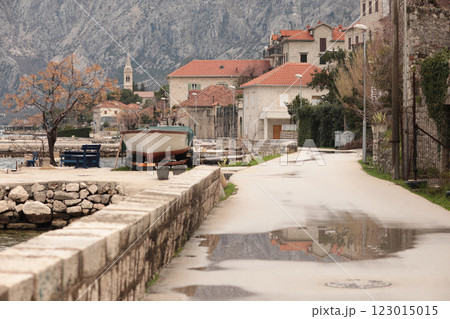 Picturesque coastal road lined with historic buildings and a moored boat in a serene bay of Montenegro 123015015