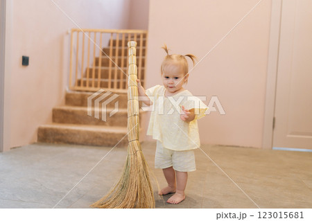 Portrait of barefoot toddler girl cleaning kitchen floor, gripping broom handle while assisting with housework in contemporary home setting, developing early sense of responsibility. Portrait of barefoot toddler girl cleaning kitchen floor, gripping broom handle while assisting with housework in contemporary home setting, developing early sense of responsibility. 123015681