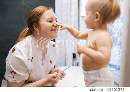 Cheerful toddler girl playfully touching nose with finger to mother in bathroom, sharing joyful morning hygiene routine. Loving smiling mom helping daughter brushing teeth together. Cheerful toddler girl playfully touching nose with finger to mother in bathroom, sharing joyful morning hygiene routine. Loving smiling mom helping daughter brushing teeth together. 123015724