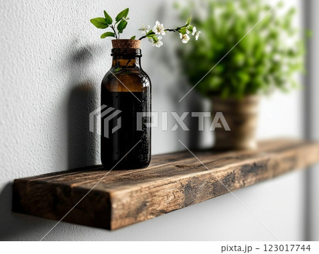 green branch delicate white blossoms rests in clear glass bottle filled water. simple arrangement is placed on wooden shelf contrasting bright white wall. 123017744