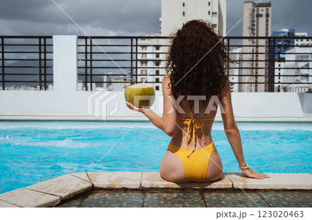 back of a young beautiful woman with a sexy body with coconut relaxing by swimming pool at a hotel in resort in summer on vacation 123020463