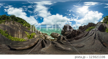 Towering granite boulders lead into the calm turquoise waters of the sea, with lush greenery draping over the rugged coastline under a sunny sky. Anse Source d'Argent. La Digue, Seychelles. VR 360. 123021106