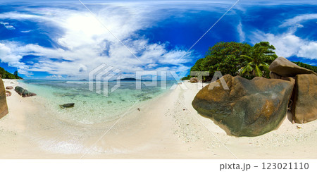 A serene beach with crystal-clear shallow waters, smooth boulders, and lush tropical vegetation, set against a vibrant blue sky. Anse Gaulettes. La Digue, Seychelles. VR 360. A serene beach with crystal-clear shallow waters, smooth boulders, and lush tropical vegetation, set against a vibrant blue sky. Anse Gaulettes. La Digue, Seychelles. VR 360. 123021110