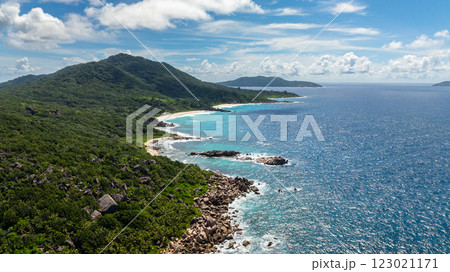 Granite rocks scattered along the coastline meet turquoise waters, bordered by lush greenery and white sands. Seychelles, La Digue. 123021171
