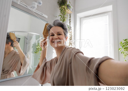 Elderly European woman pensioner middle age smiles and combs her gray hair with wooden comb. 123023092