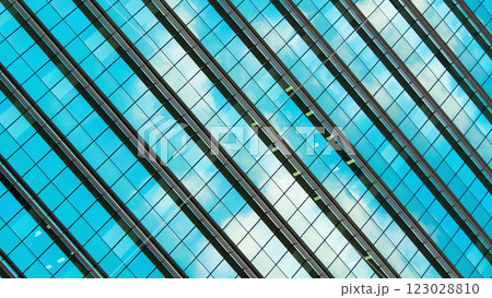 the sleek, geometric design of a building with blue-tinted glass panels. The reflection of the sky and clouds adds a dynamic and vibrant contrast to the otherwise orderly, repetitive patterns of the 123028810