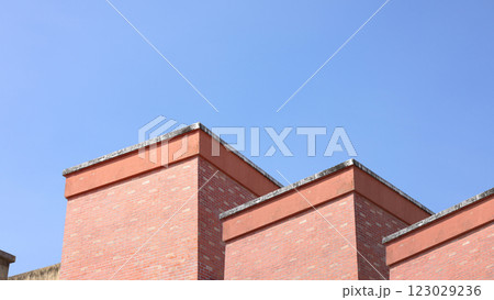 Red brick apartment building with sky, Shapes and simplicity of architecture, Fragment of roof of modern private dwelling house against of sky, Blue sky and Sunlight in background with copy space. Red brick apartment building with sky, Shapes and simplicity of architecture, Fragment of roof of modern private dwelling house against of sky, Blue sky and Sunlight in background with copy space. 123029236