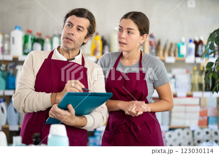 Man and girl sellers, with paper and invoice in hands, make inventory in store. Man and girl sellers, with paper and invoice in hands, make inventory in store. 123030114