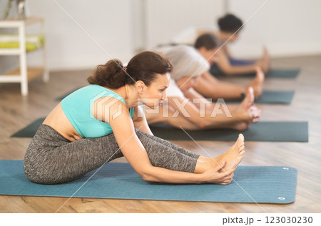 Woman stretching in Paschimottanasana during group yoga class 123030230