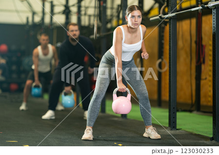 Sporty girl performing exercises with kettlebells during intense group workout 123030233