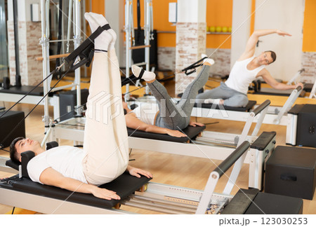 Man works out in gym and performs set of exercises to stretch leg muscles with help of reformer 123030253