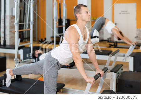 Man performing pilates exercises on reformer in fitness studio 123030375