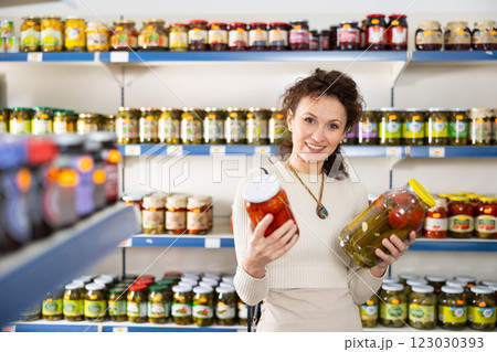 In Russian goods store, woman choose jar of pickled tomatoes and cucumbers In Russian goods store, woman choose jar of pickled tomatoes and cucumbers 123030393