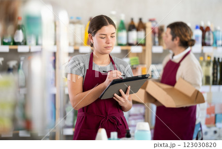 Female manager makes notes on an electronic tablet - conducts an inventory. In background, male salesperson places goods on shelves Female manager makes notes on an electronic tablet - conducts an inventory. In background, male salesperson places goods on shelves 123030820