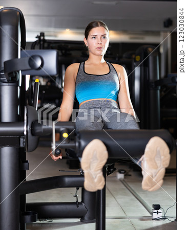 Slender athletic girl work out muscles of legs and thighs on simulator in fitness club 123030844
