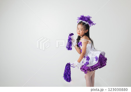 Cheerful young cheerleader girl in a purple and white outfit, holding pom-poms. Energetic studio shot on a white background, full of joy and excitement. cheerleader kid 123030880