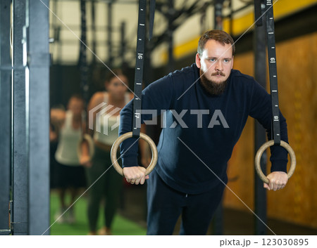 Bearded guy performing push-ups in gymnastic rings at gym Bearded guy performing push-ups in gymnastic rings at gym 123030895