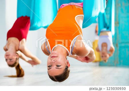 Girl doing dove pose in hanging hammock during aerial yoga group workout Girl doing dove pose in hanging hammock during aerial yoga group workout 123030930