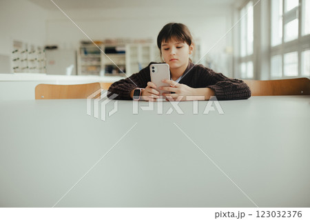 Young schoolgirl sitting in a science lab with a phone in her hand, waiting for classmates. Young schoolgirl sitting in a science lab with a phone in her hand, waiting for classmates. 123032376