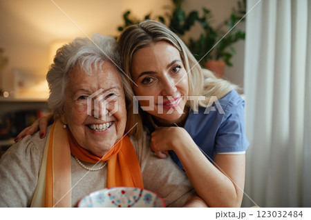 Portrait of smiling nurse and a senior patient, hugging her during visit at home. 123032484