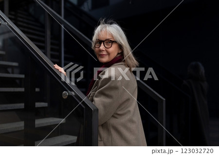 Elderly businesswoman standing confidently on stairs outside a modern office during the daytime Elderly businesswoman standing confidently on stairs outside a modern office during the daytime 123032720