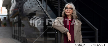 Middle-aged Caucasian businesswoman poses confidently at a modern urban office building on a sunny Middle-aged Caucasian businesswoman poses confidently at a modern urban office building on a sunny 123032721